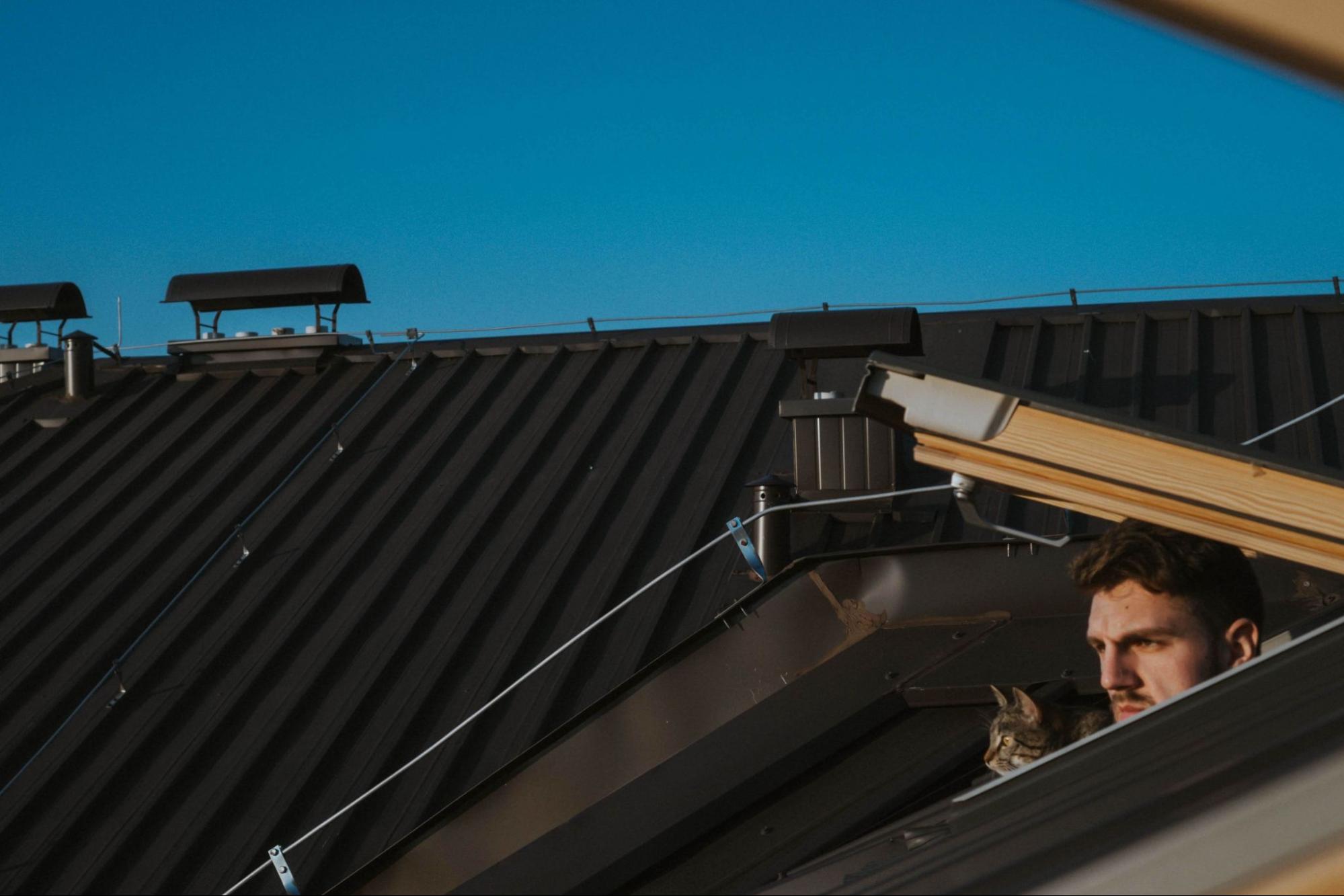 Young Caucasian man with his tabby cat on the roof near a scupper.