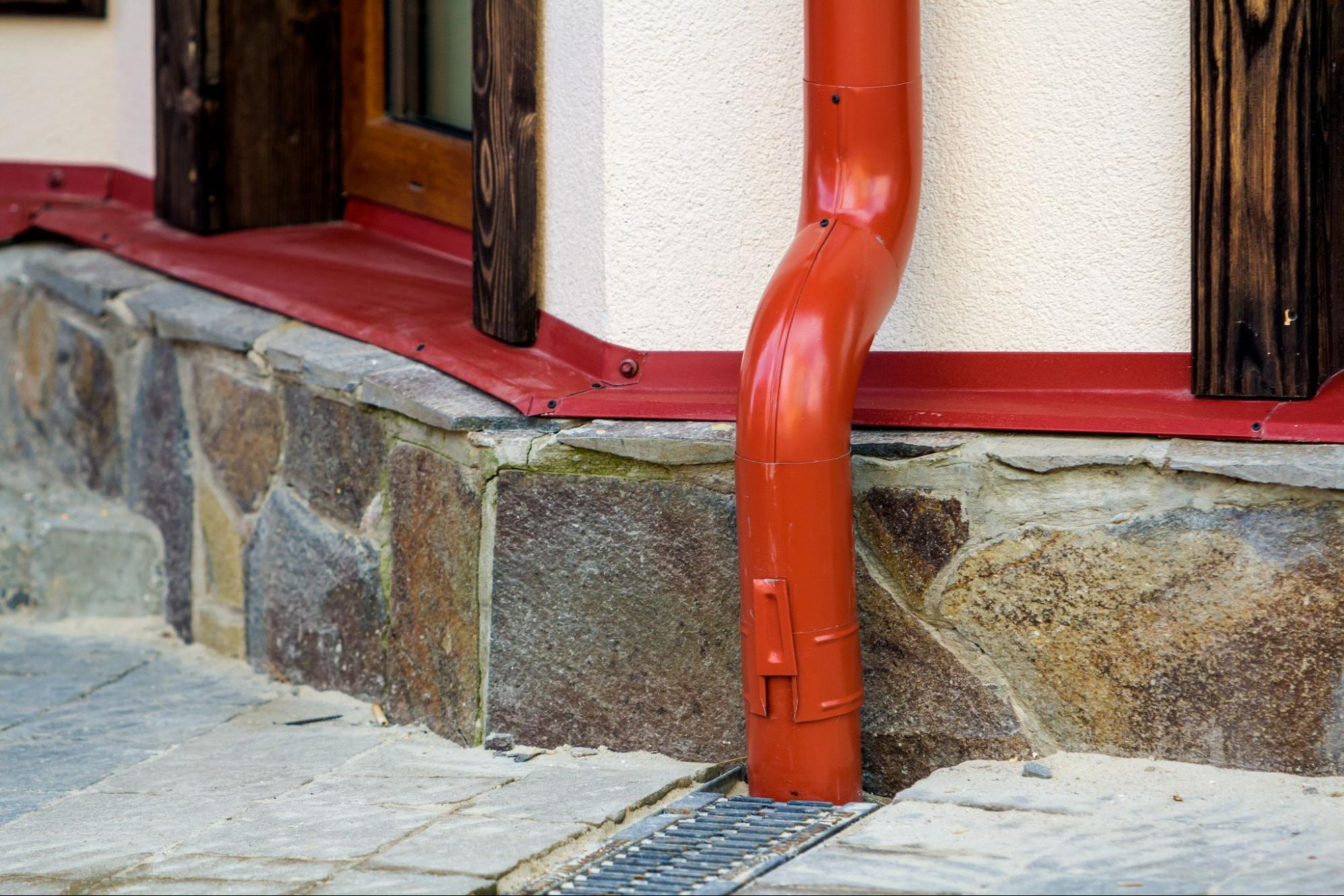A red metal downspout connected to the gutter system of a new house.