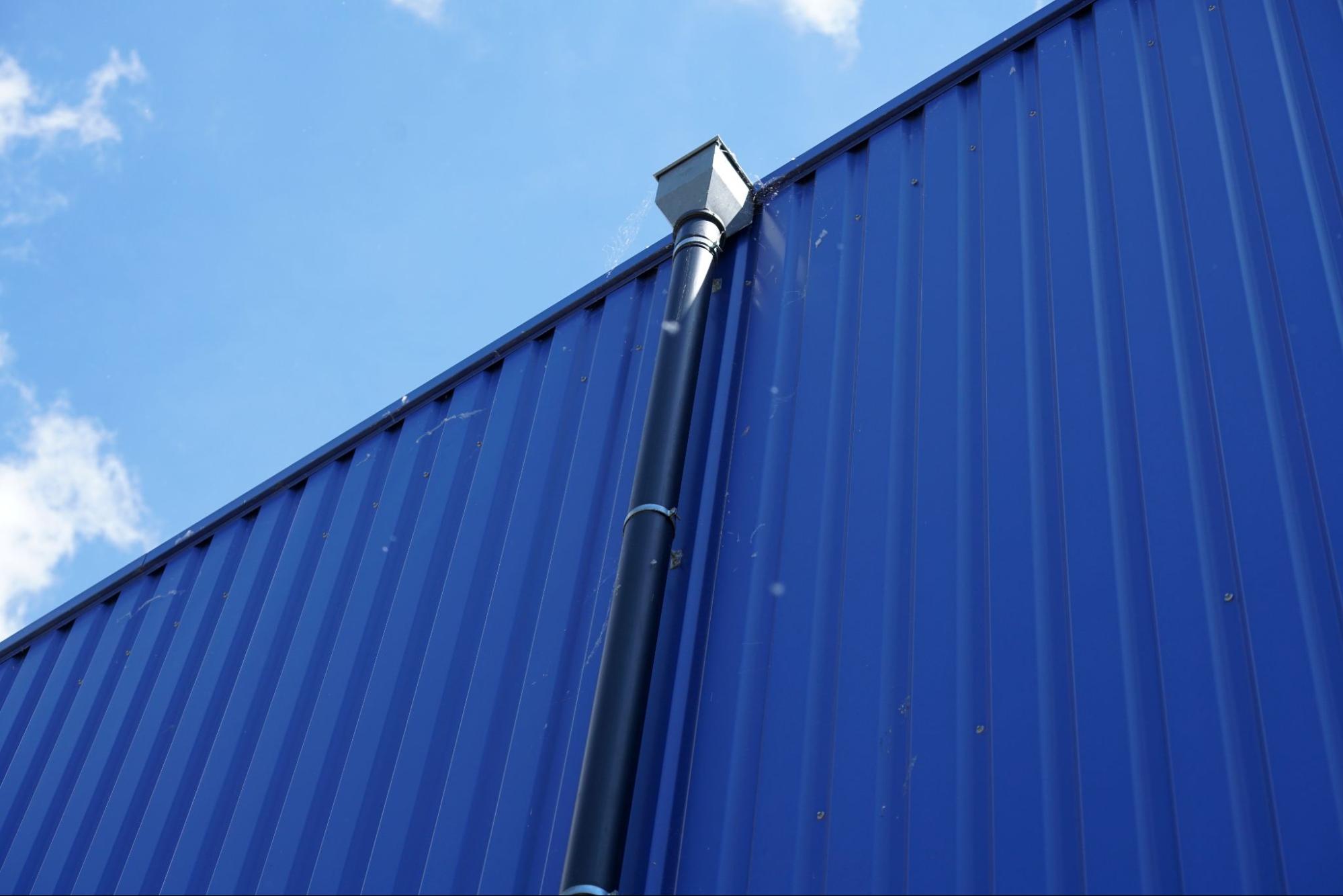 Black downspout attached to a blue metal commercial wall.