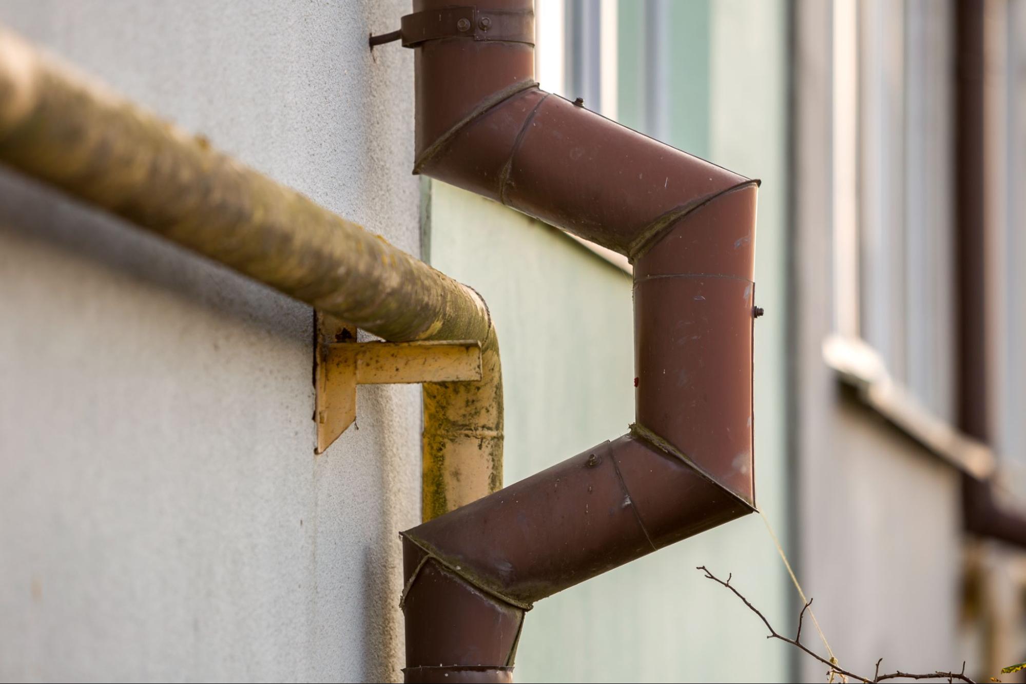 Detailed close-up of an old gas pipe and a newly painted brown roof gutter