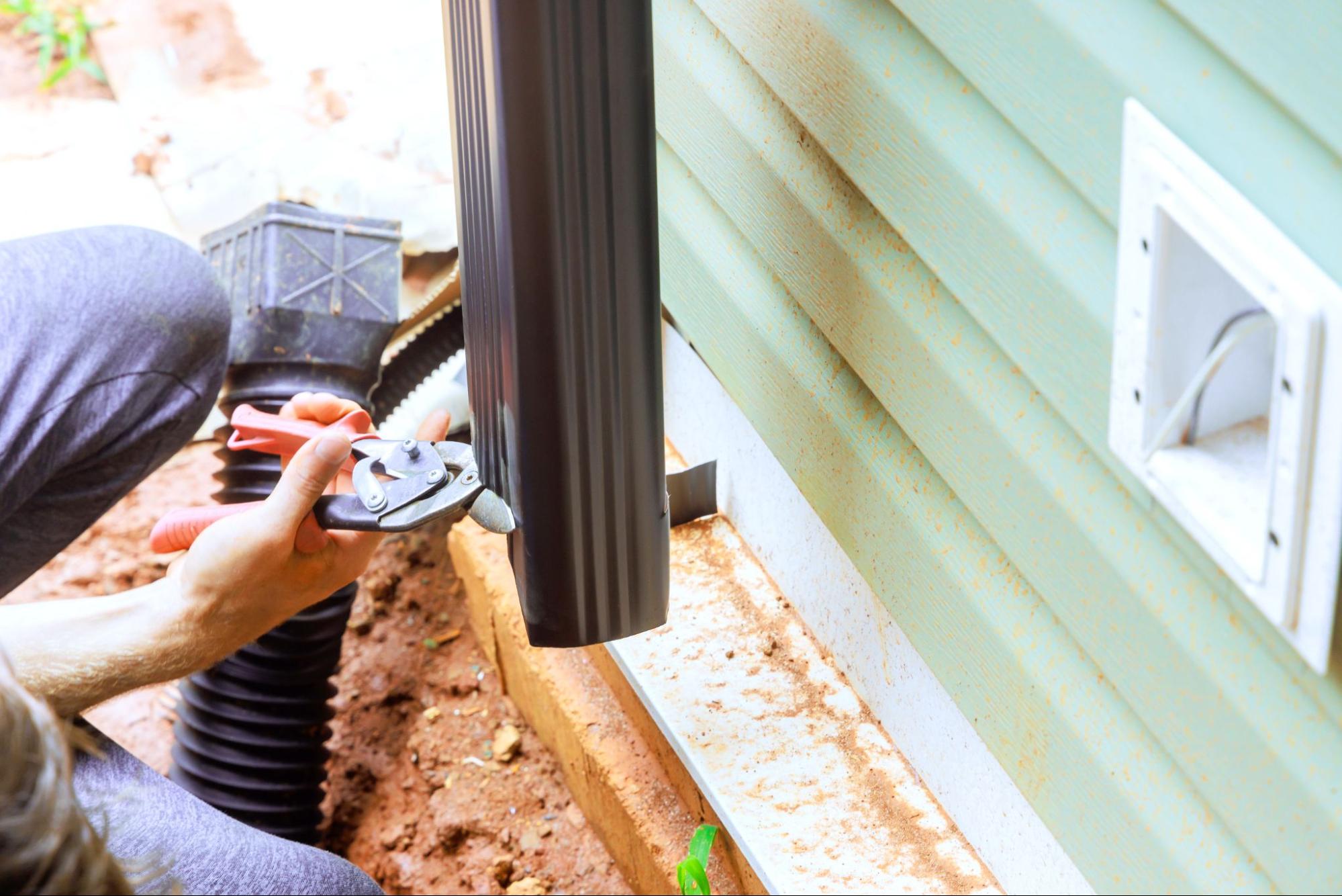 Close-up view of a worker installing a metal downspout to the roof gutter system