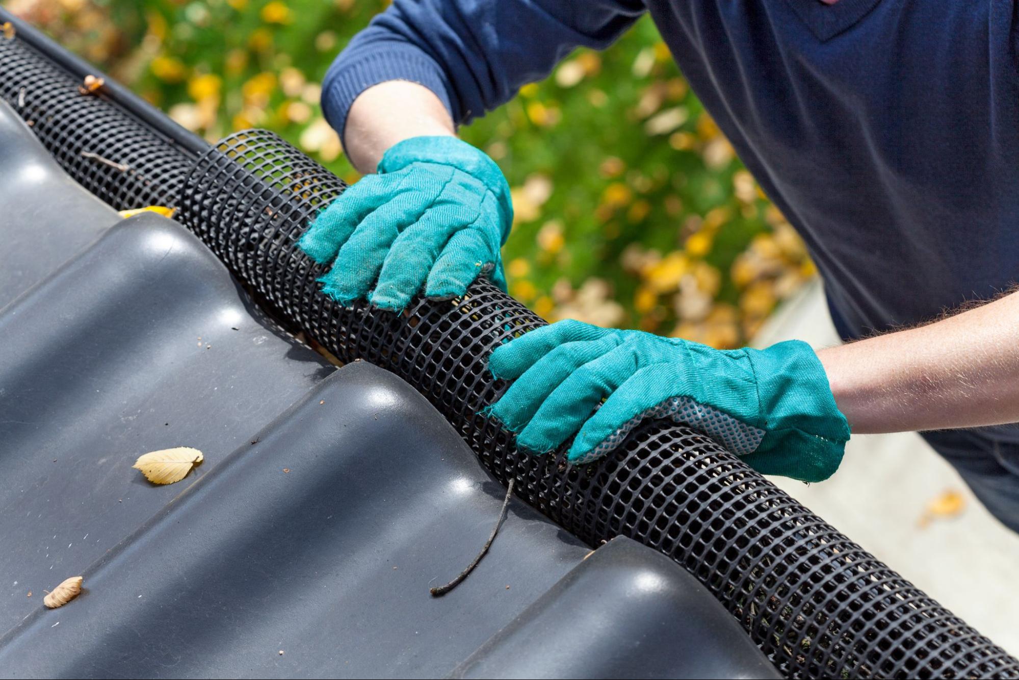 Close-up of hands in glovesfitting a black net on a roof gutter for protection