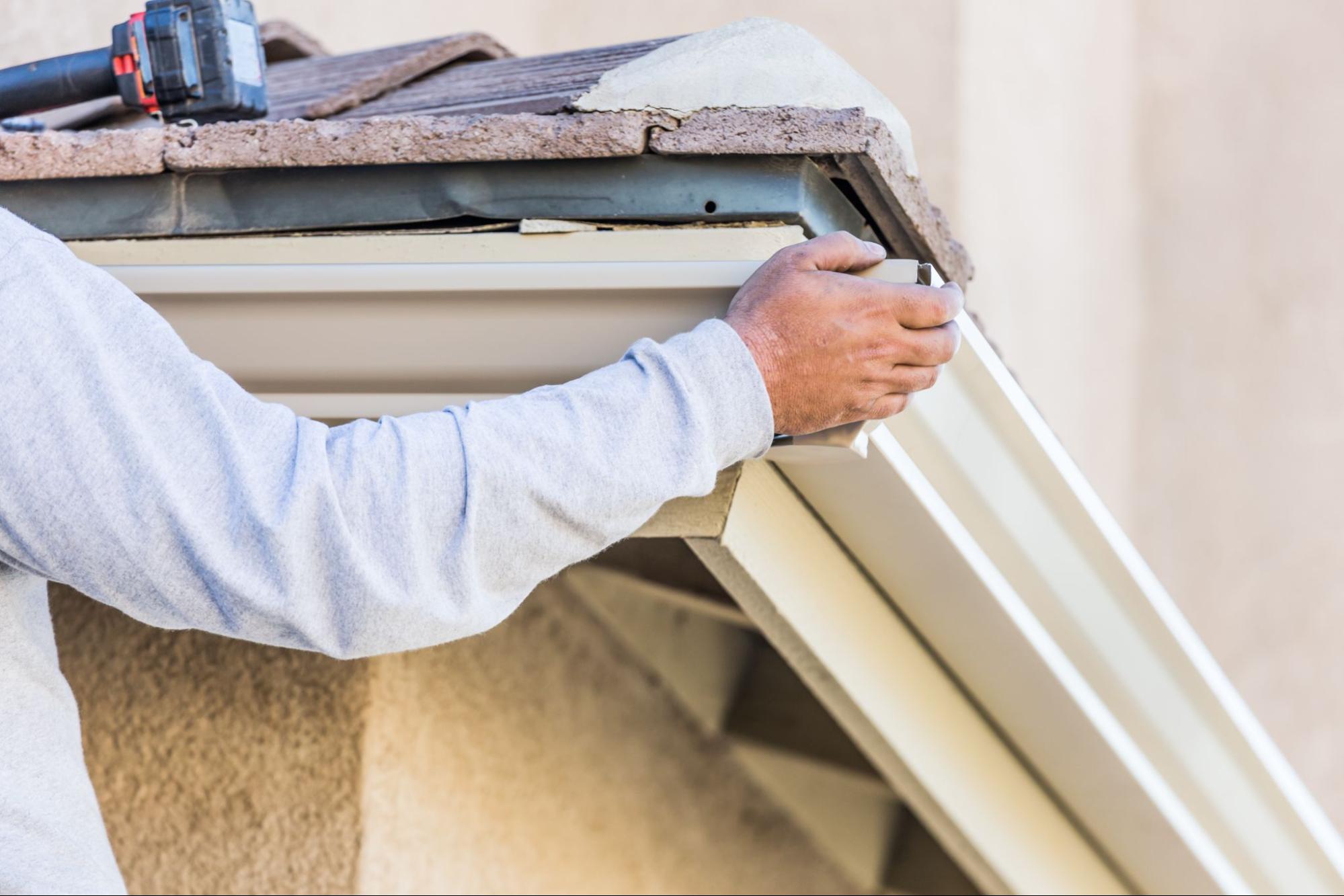 A contractor performing gutter repair with a power tool on a house exterior