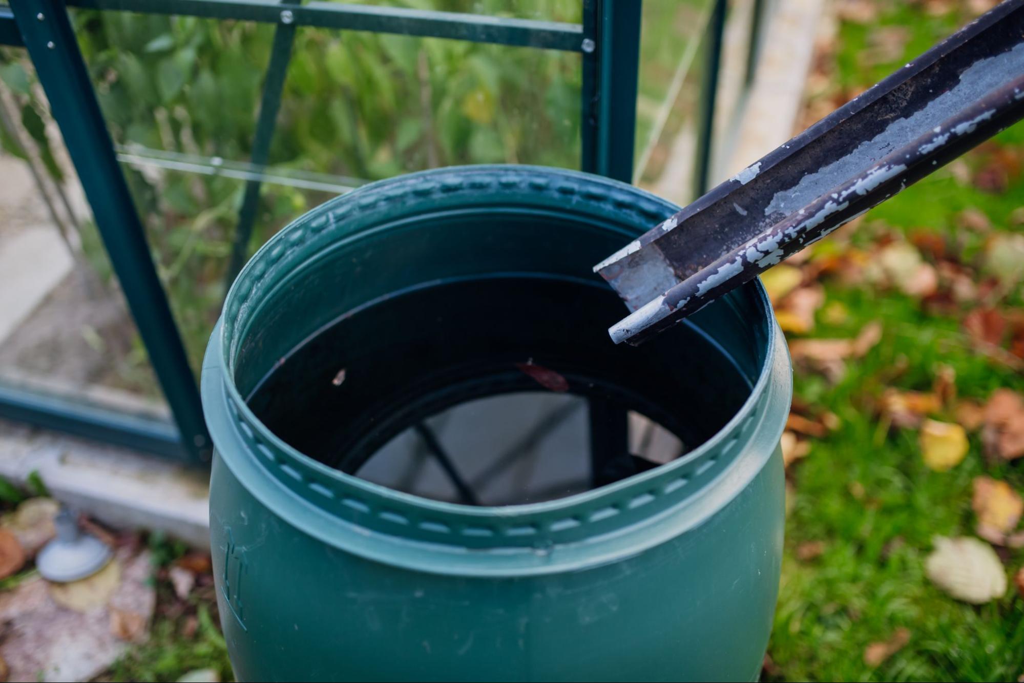 Overhead view of rain barrel under downspout collecting roof runoff in garden