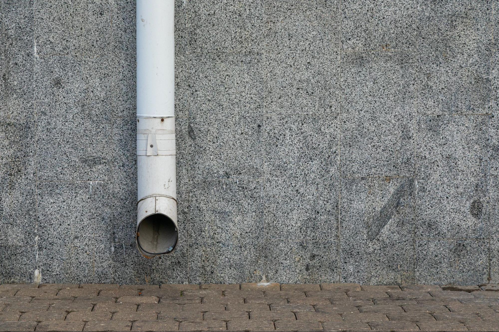 Drain pipe installed along a granite wall and brick surface