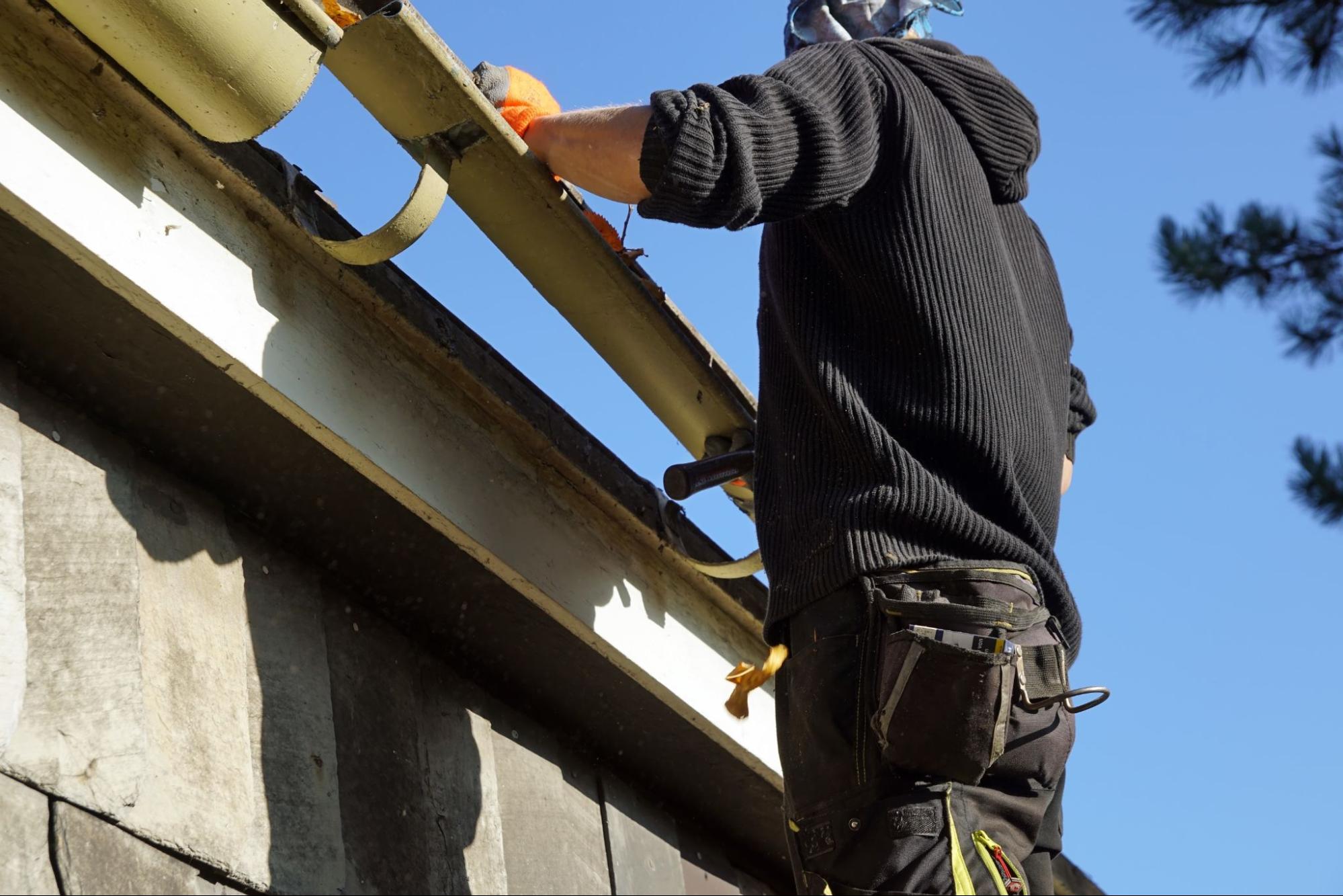 Worker removing leaves from gutters on a residential home roof