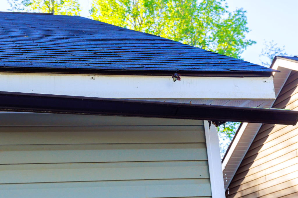 Detached gutter pulling away from the roof edge with green trees in the background