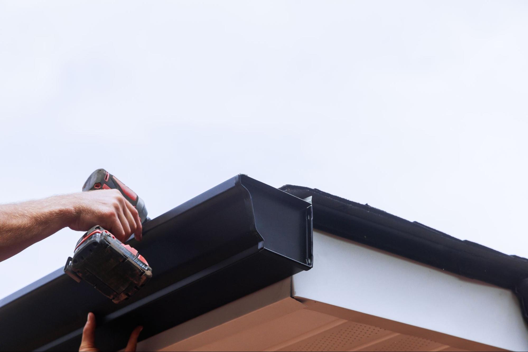 Local gutter installer securing gutters to a roof using a power drill during installation