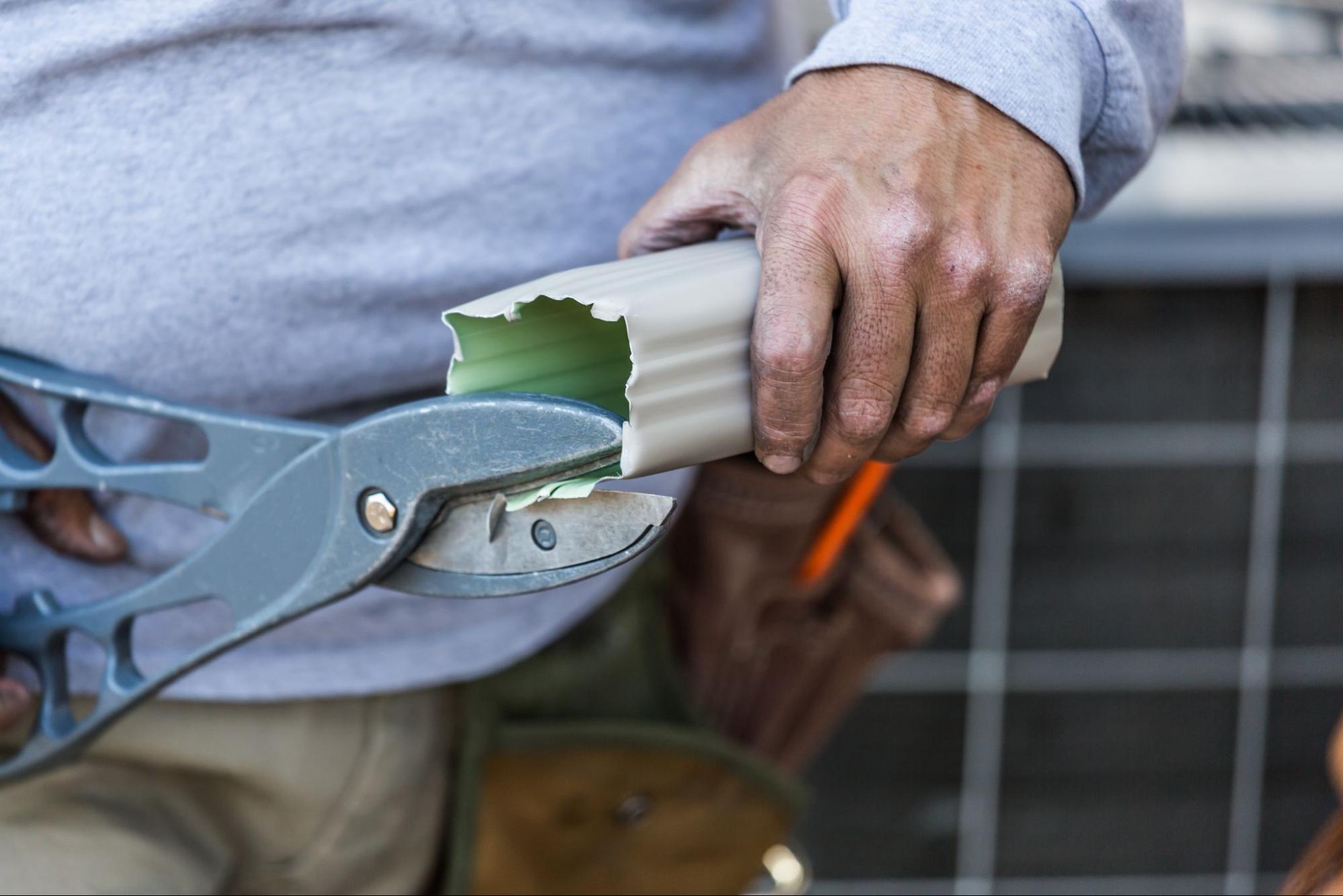 Close-up of a worker cutting a rain gutter with tin snips at a job site