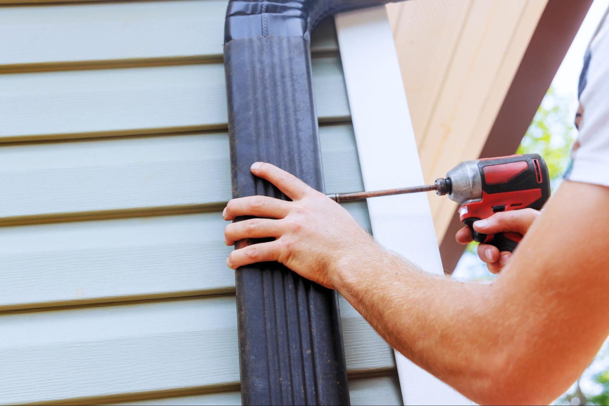 Contractor securing gutter system to exterior wall with a power drill