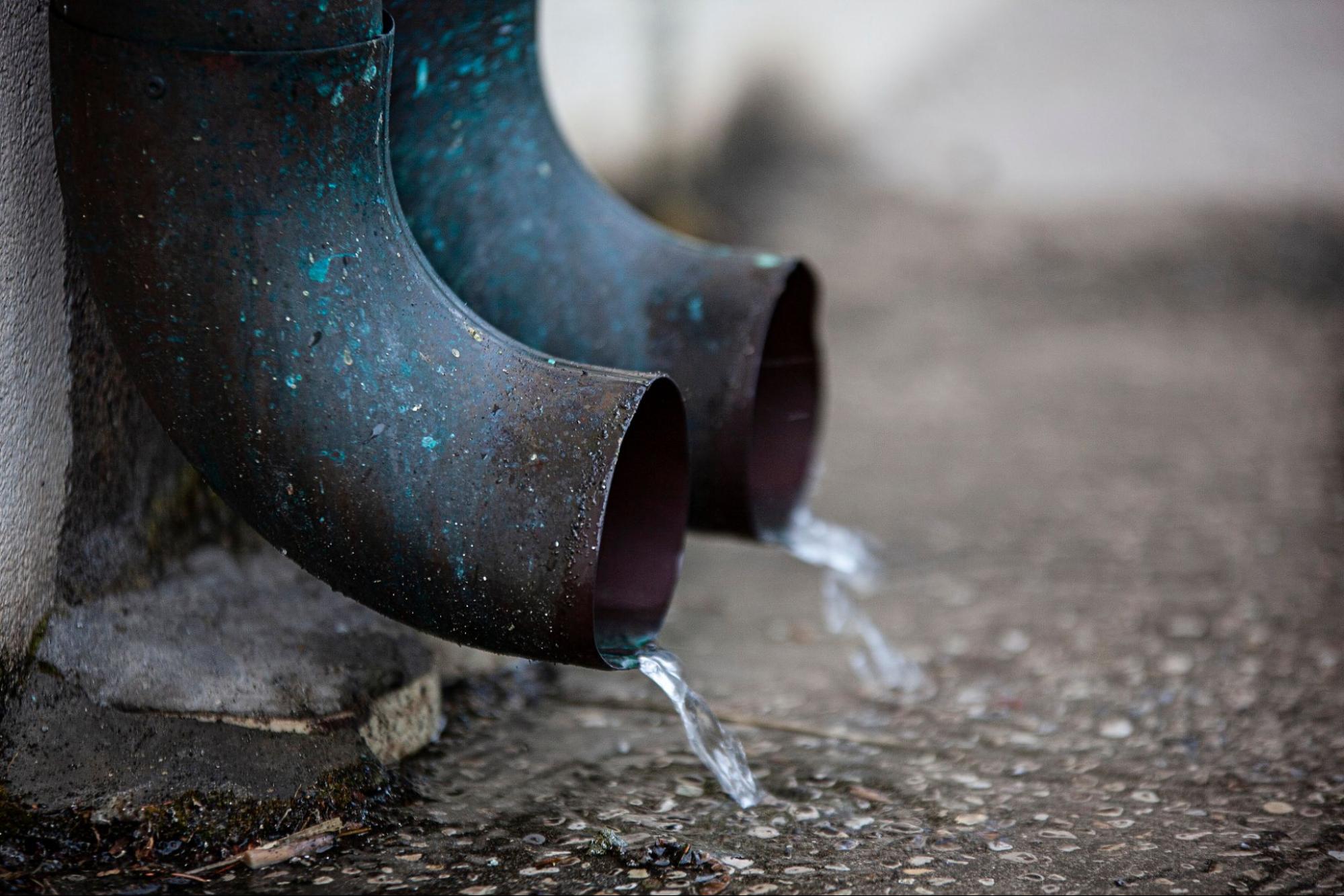 Drainage pipe releasing water onto a concrete surface near the foundation