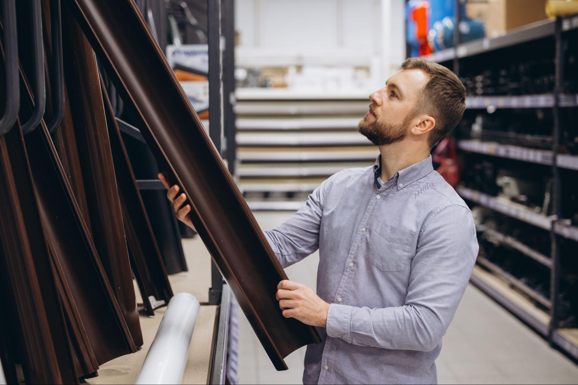 Man comparing gutter profiles and home drainage materials inside a hardware store