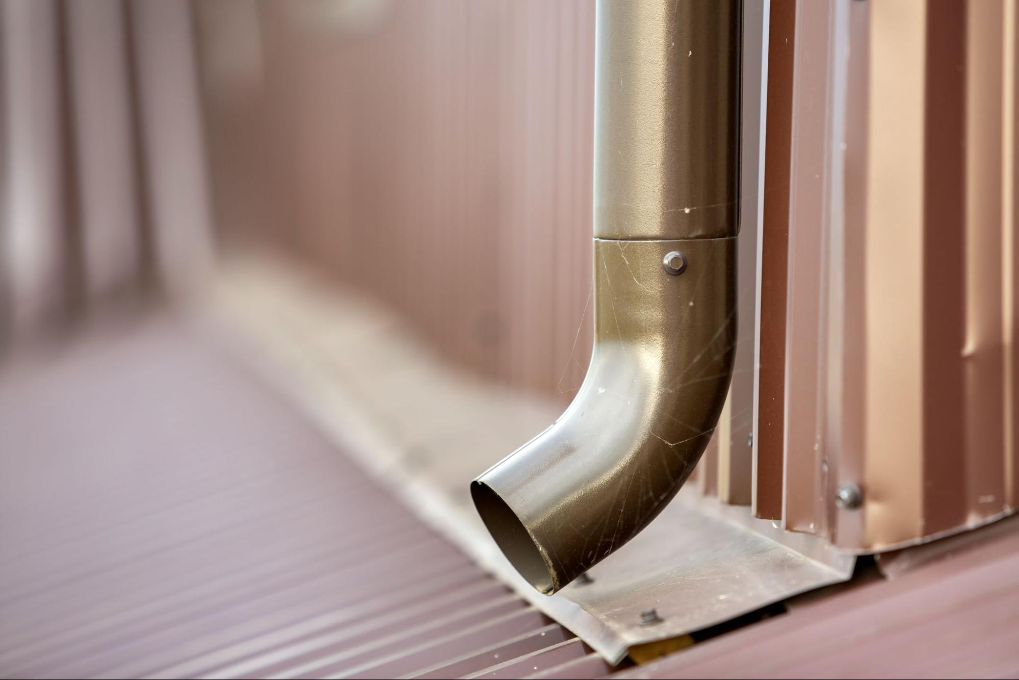 Close-up of a drainage pipe on a ribbed roof directing rainwater
