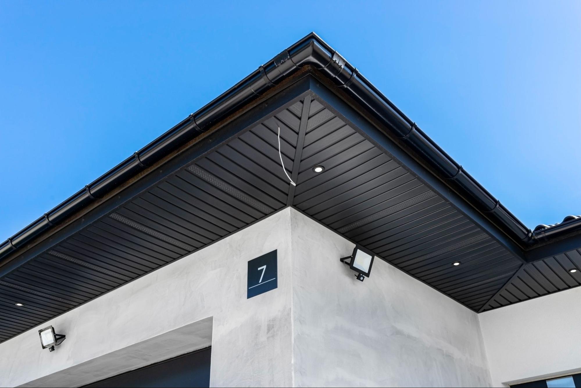 Modern building exterior under a clear blue sky with professional rain gutter installation along the roofline.