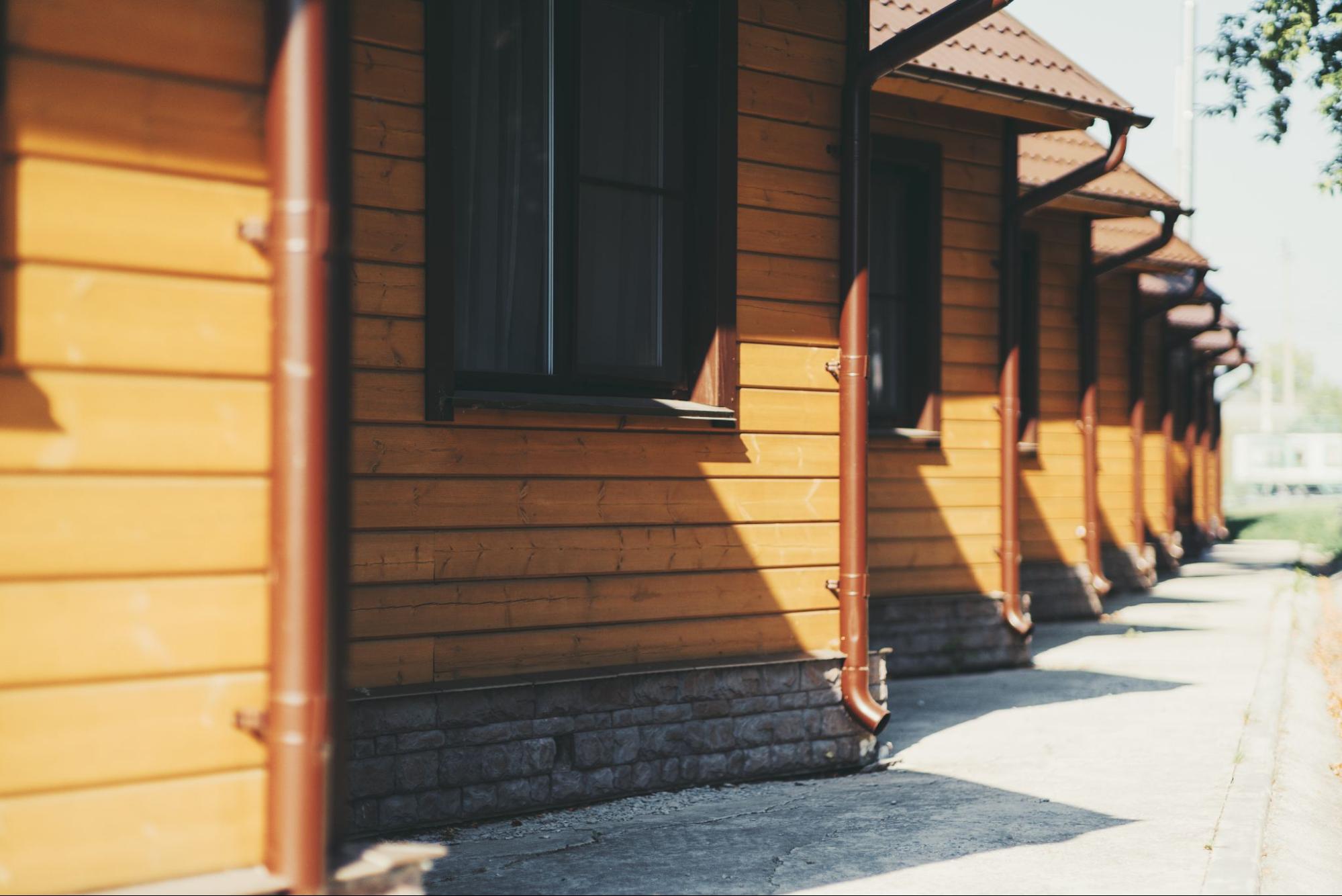 Row of yellow wooden houses with newly installed metal downspouts directing rainwater away from the foundations
