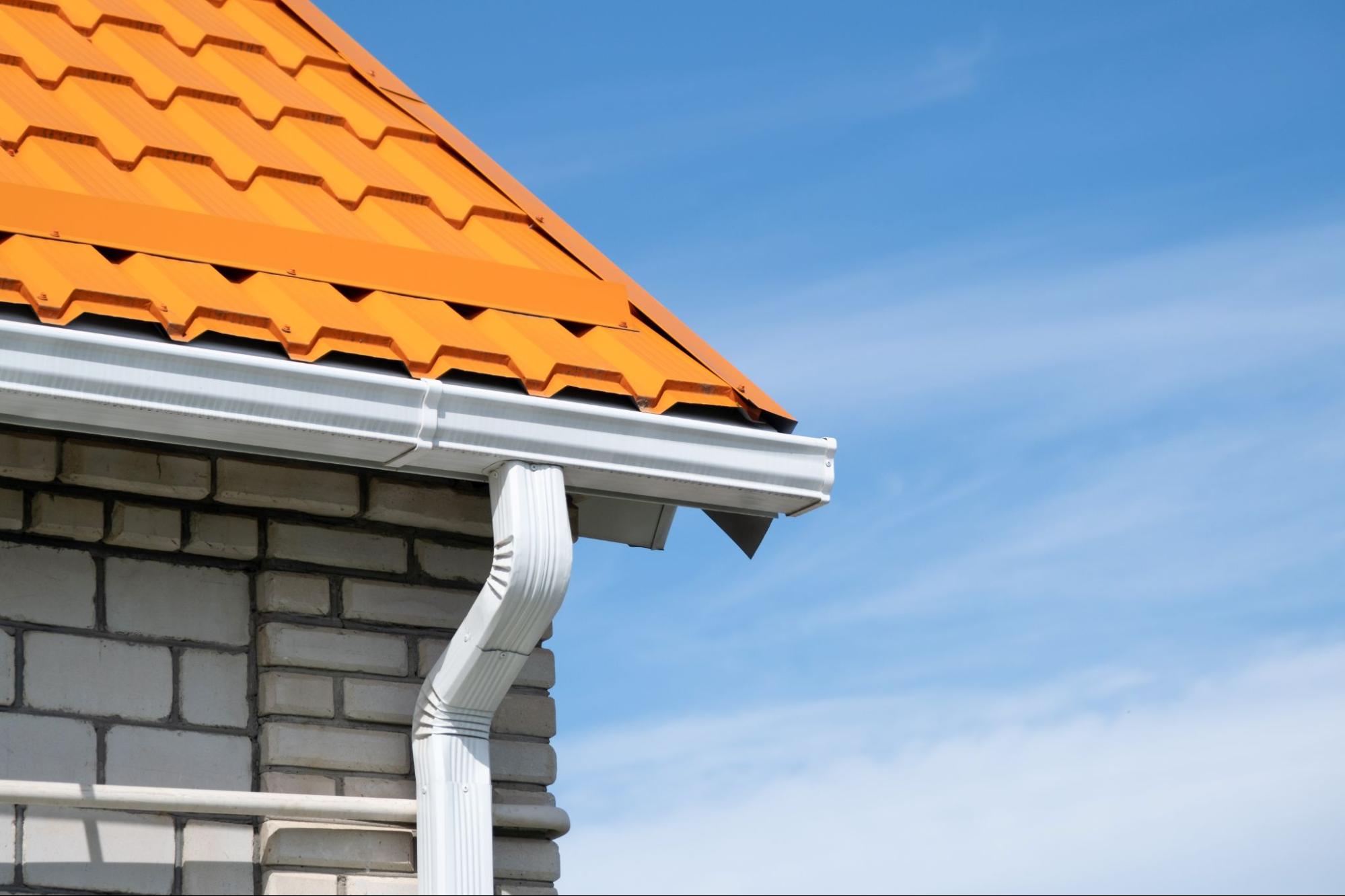 Orange tile roof with white rain gutters installed along the building exterior