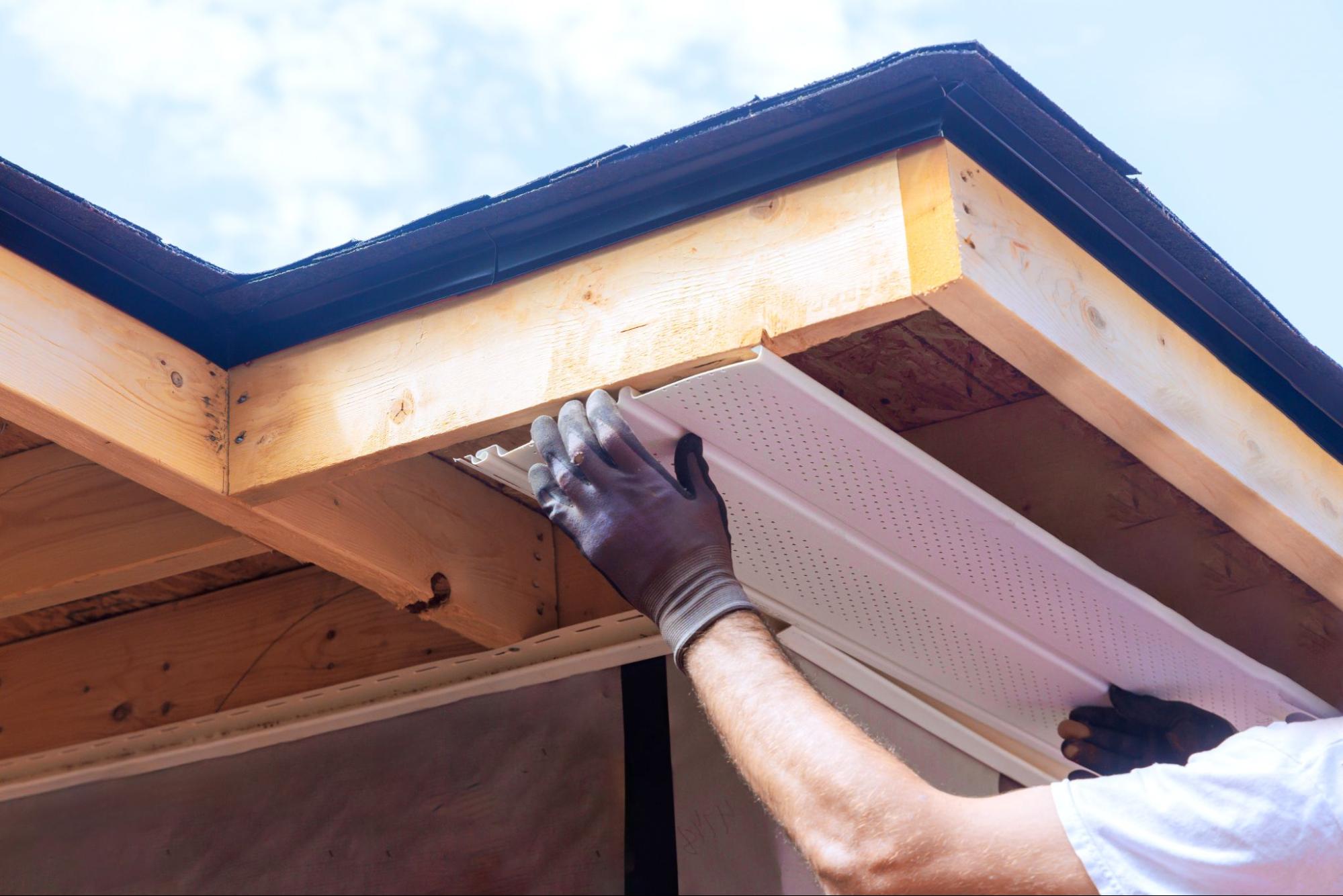 Worker installing soffit panels beneath the roof eaves of a residential home
