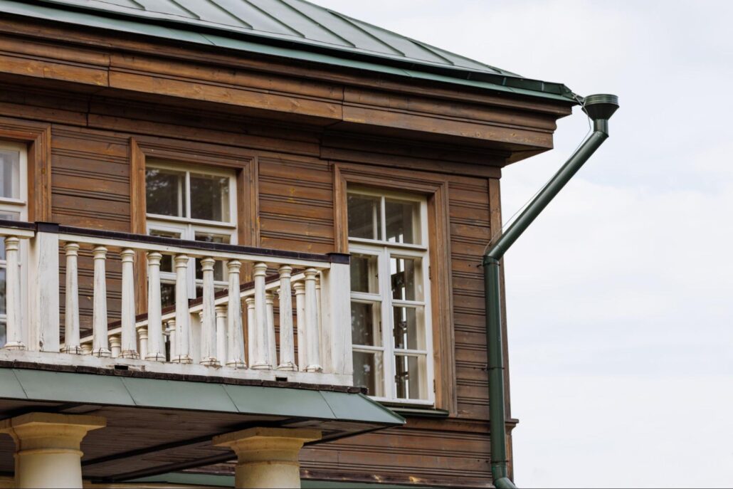 Wooden building with balcony and downspout drainage directing roof runoff away from the structure