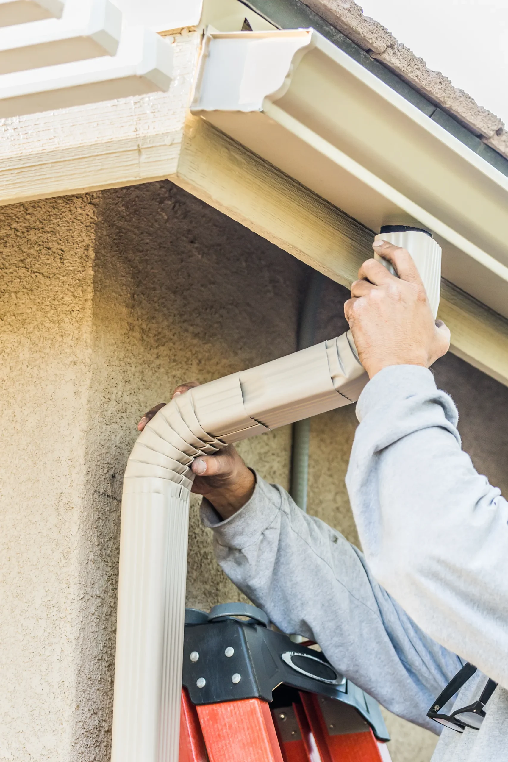 Worker's hands installing or replacing a new downspout onto a house gutter, focusing on the connection point.
