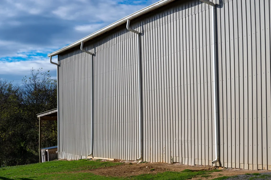 Side view of a large industrial or commercial building with corrugated metal siding in vertical panels and a light-colored gutter system along the roofline, under a partly cloudy sky.