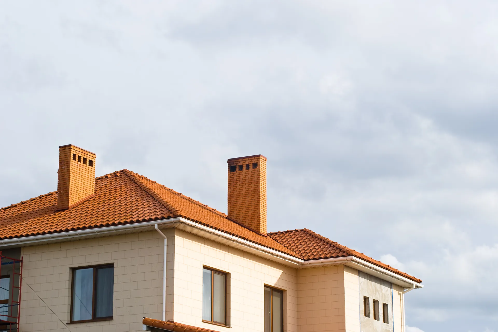 Residential house with new clay tile roof and two brick chimneys under a cloudy sky