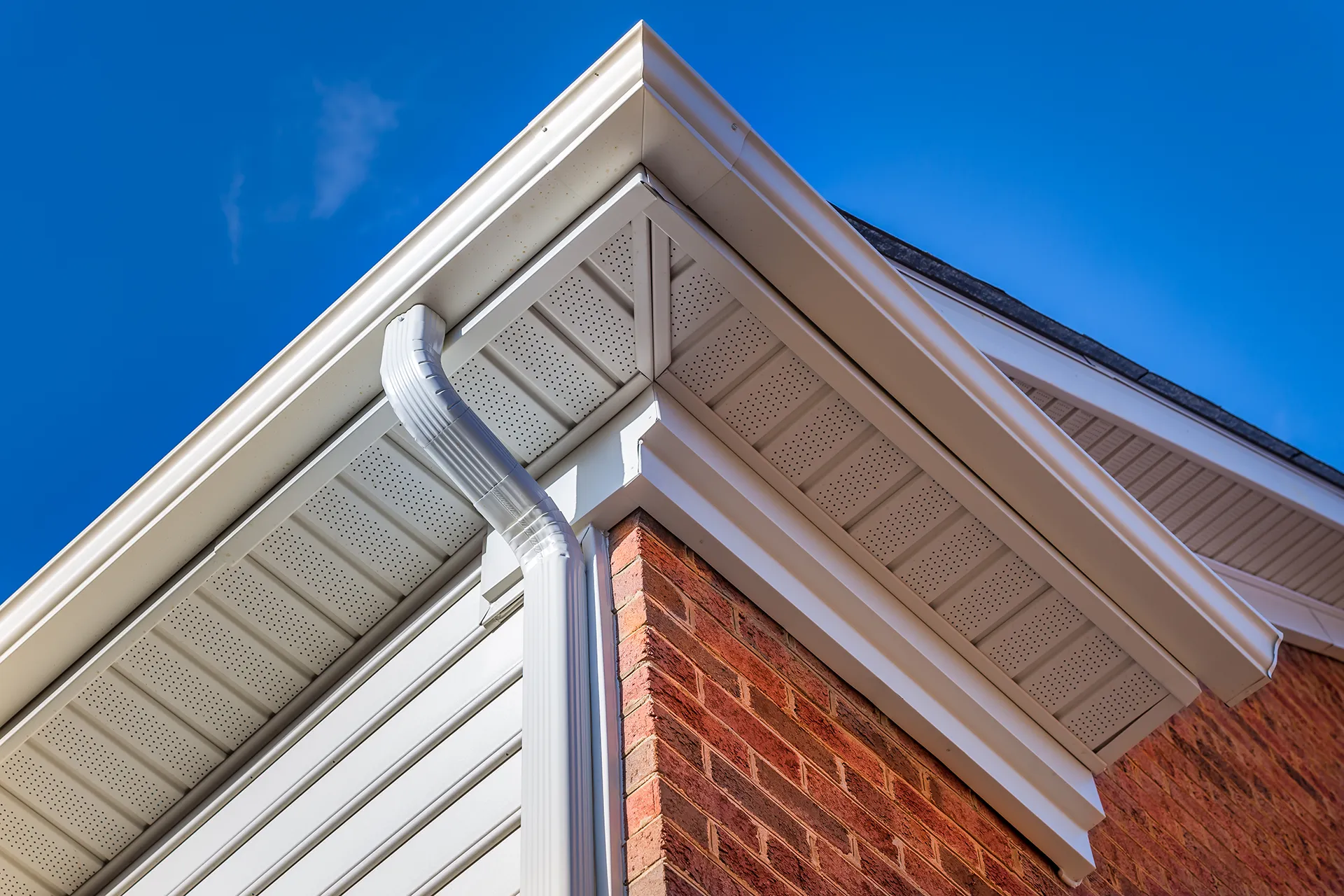 Close-up of white seamless rain gutters installed on house eaves with a blue sky background
