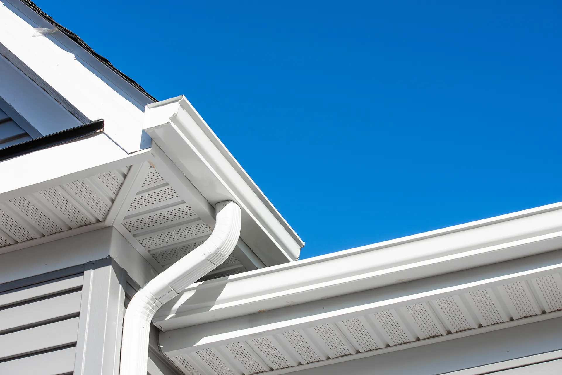 White traditional gutter and downspout system on a house against a clear blue sky
