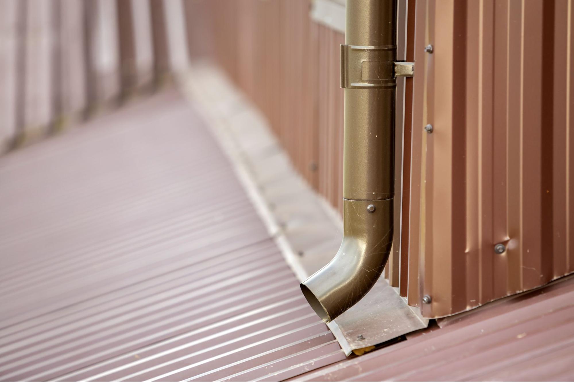 Close-up of a new brown metal downspout system mounted on a wall.