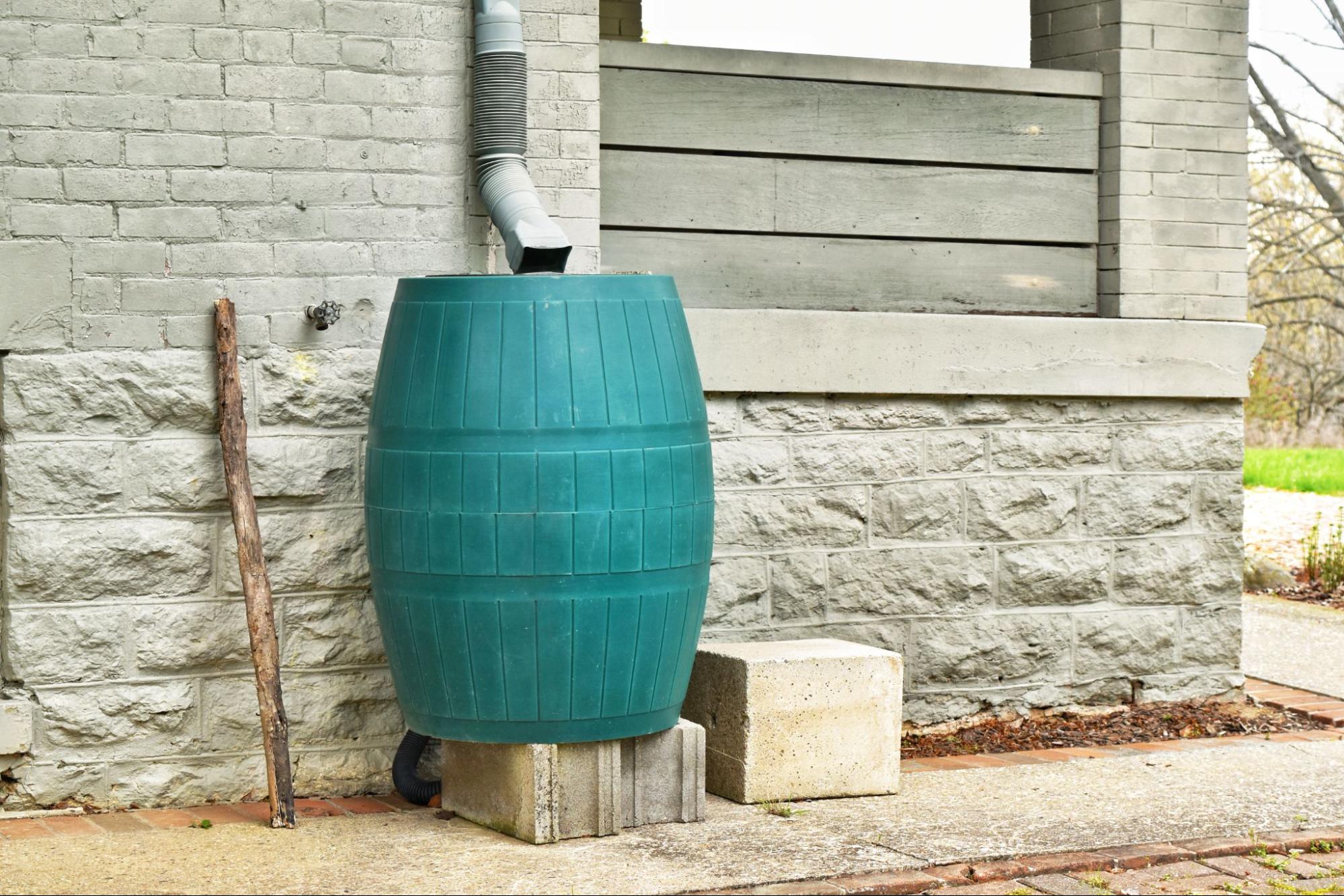 A teal rain barrel sits under a gutter on the side of a home.