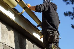 A low-angle view of a worker installing and repairing a roof gutter.
