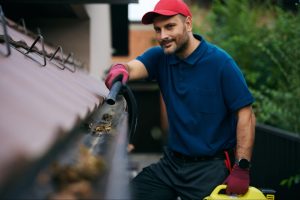 A worker uses a leaf blower to clear debris to prevent gutter overflow