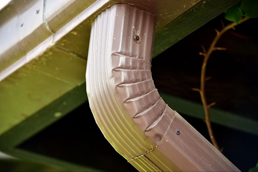Brown metal downspout connected to a gutter, directing roof runoff safely to ground drainage