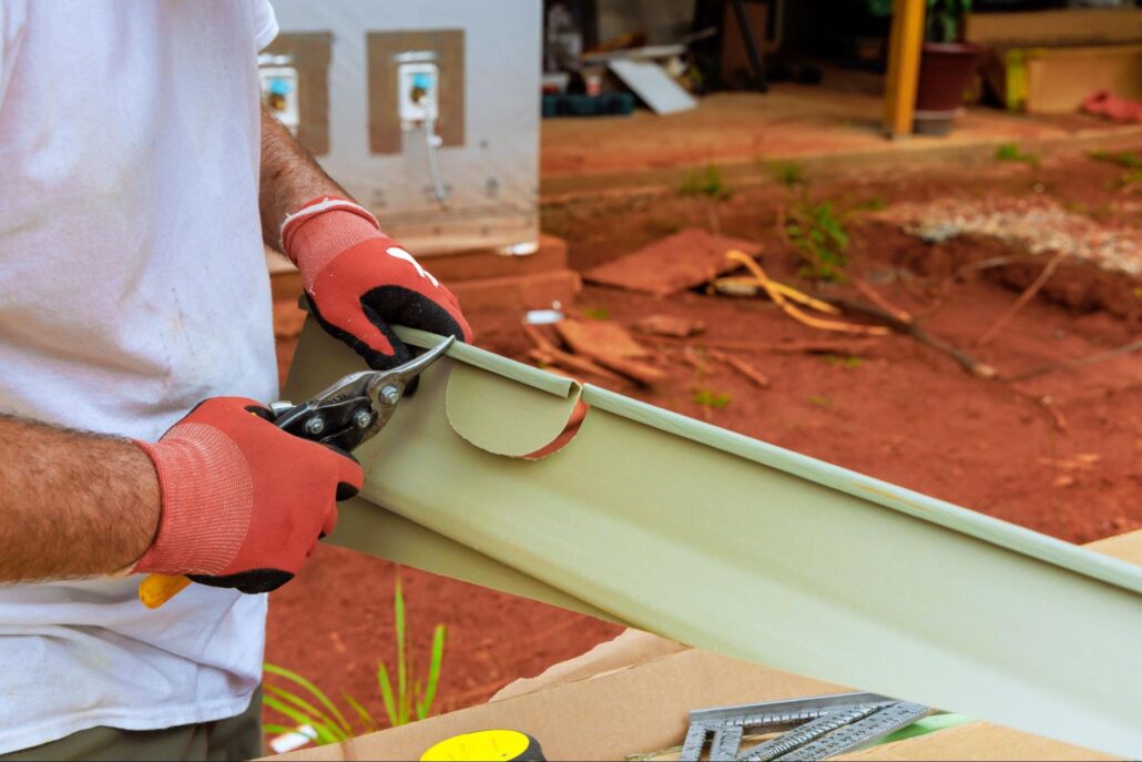 Worker cutting aluminum gutter with tin snips during on-site repair work