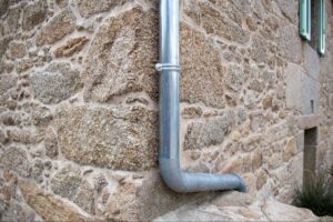 Metal downspout draining rainwater from gutter on antique stone house