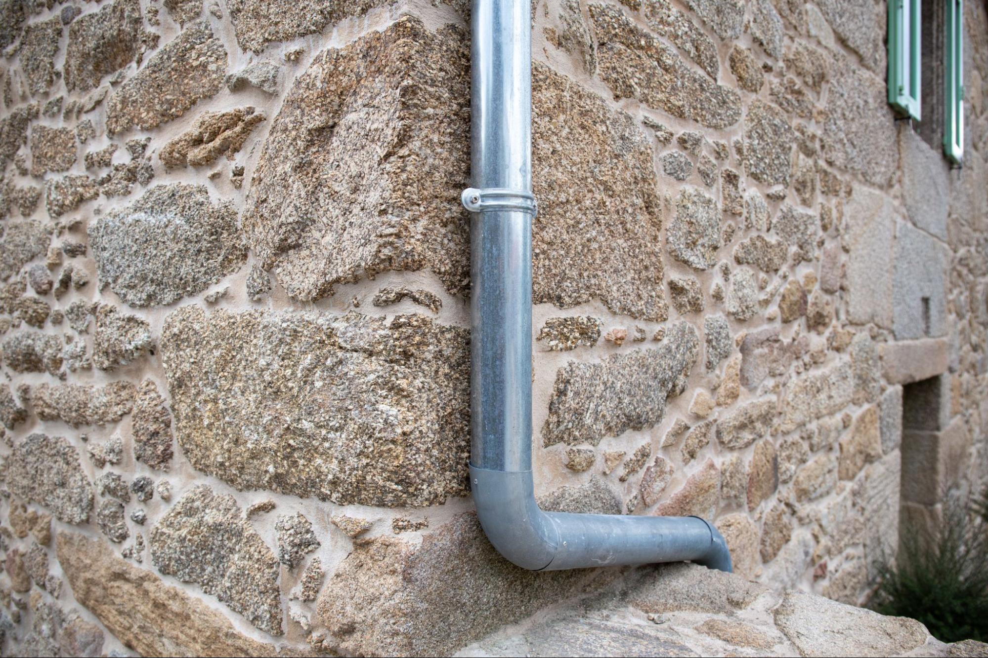 Metal downspout draining rainwater from gutter on antique stone house