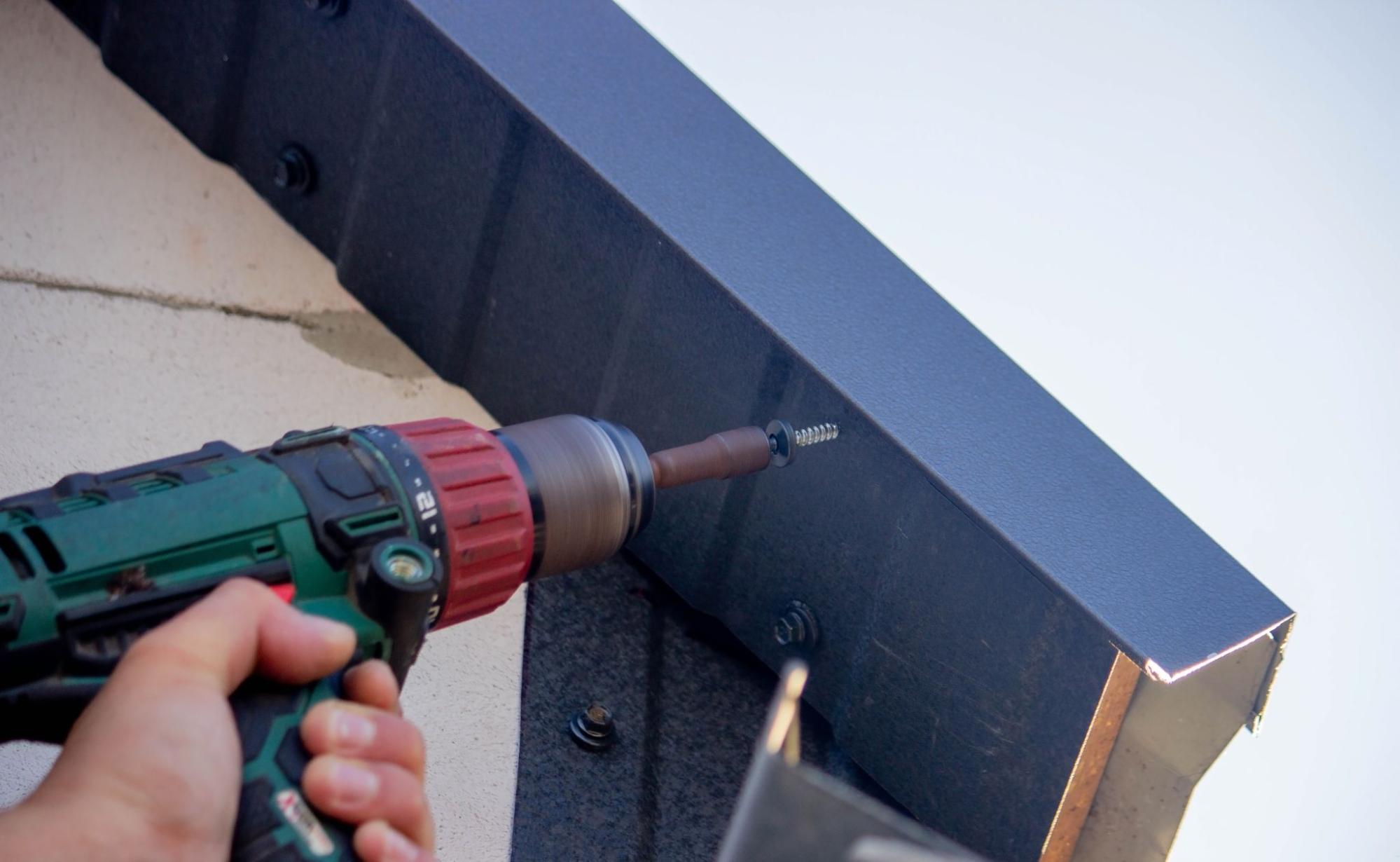 Technician securing the gutter from below by drilling a screw into place