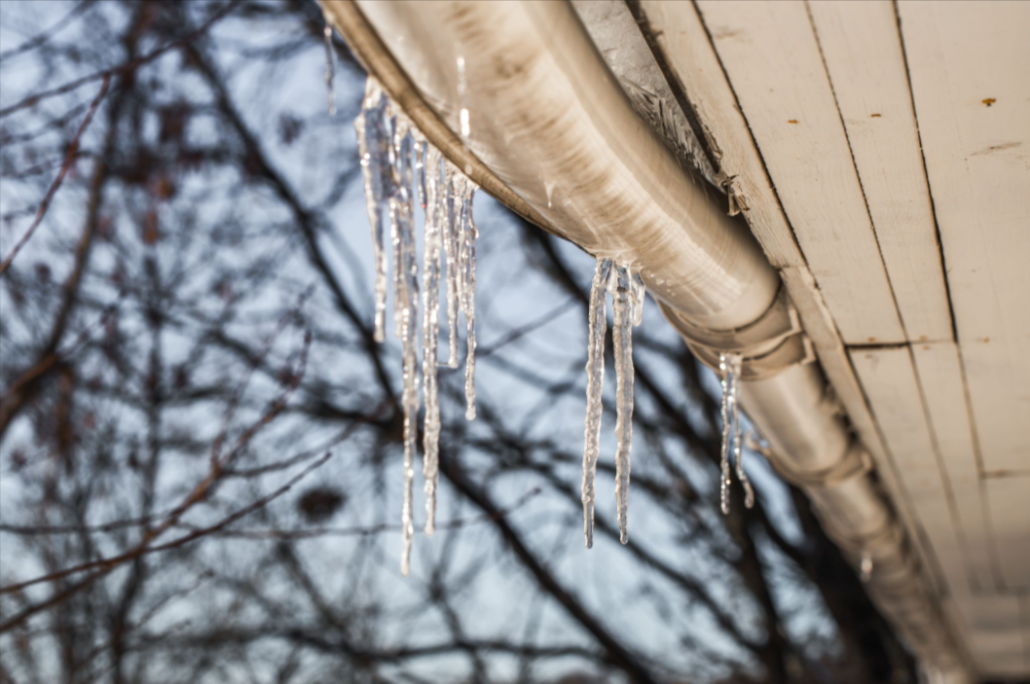 Icicles hanging from a sagging roof gutter during winter, showing ice buildup and drainage issues