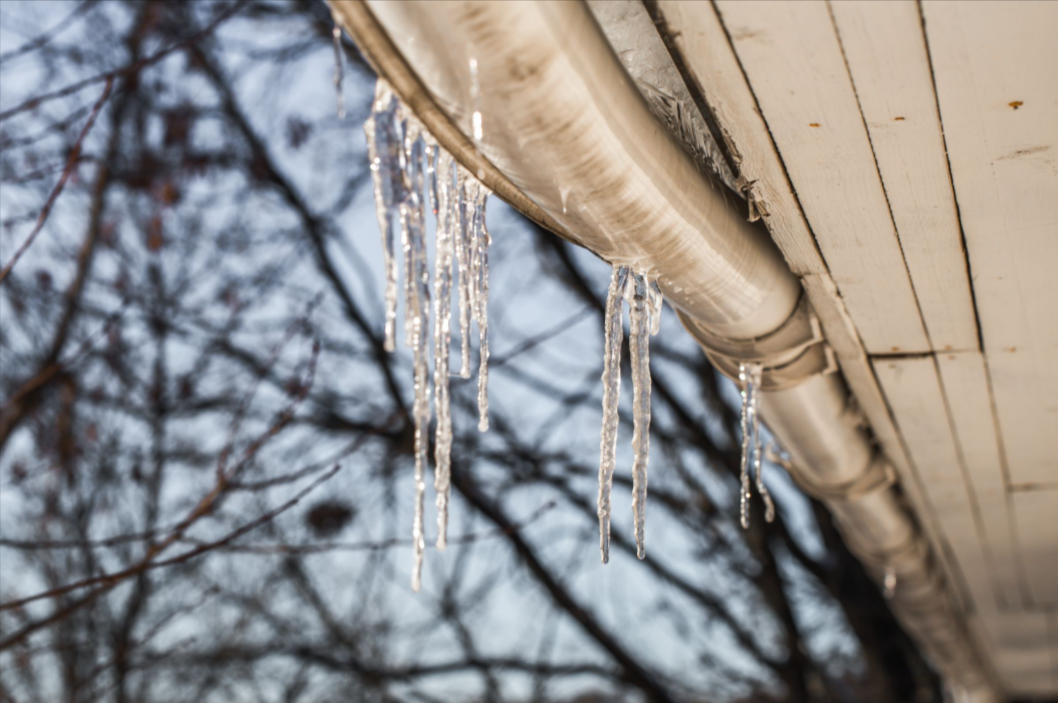 Icicles hanging from a sagging roof gutter during winter, showing ice buildup and drainage issues