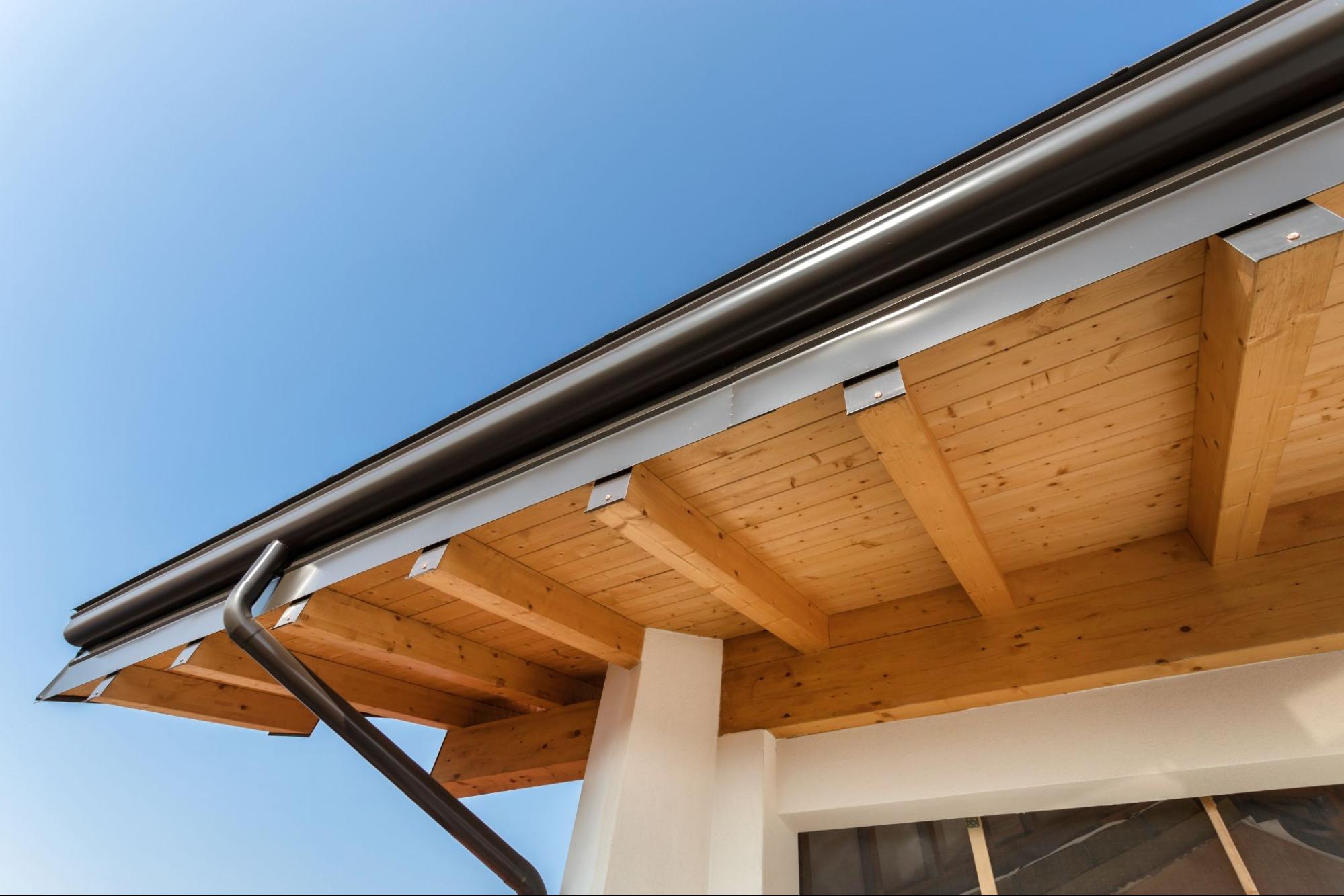 Seamless gutter system attached to a roofline with a bright blue sky in the background